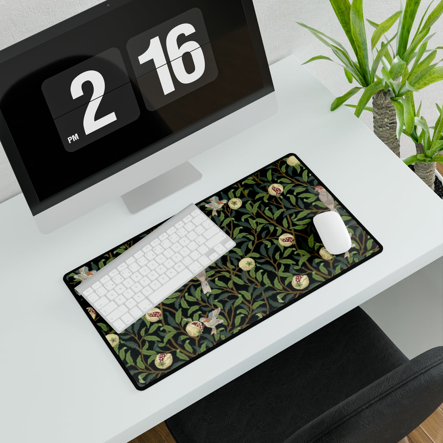 A rectangular desk mat with a floral William Morris & Co pattern featuring birds and pomegranates, placed under a desk with a keyboard and mouse on top.
