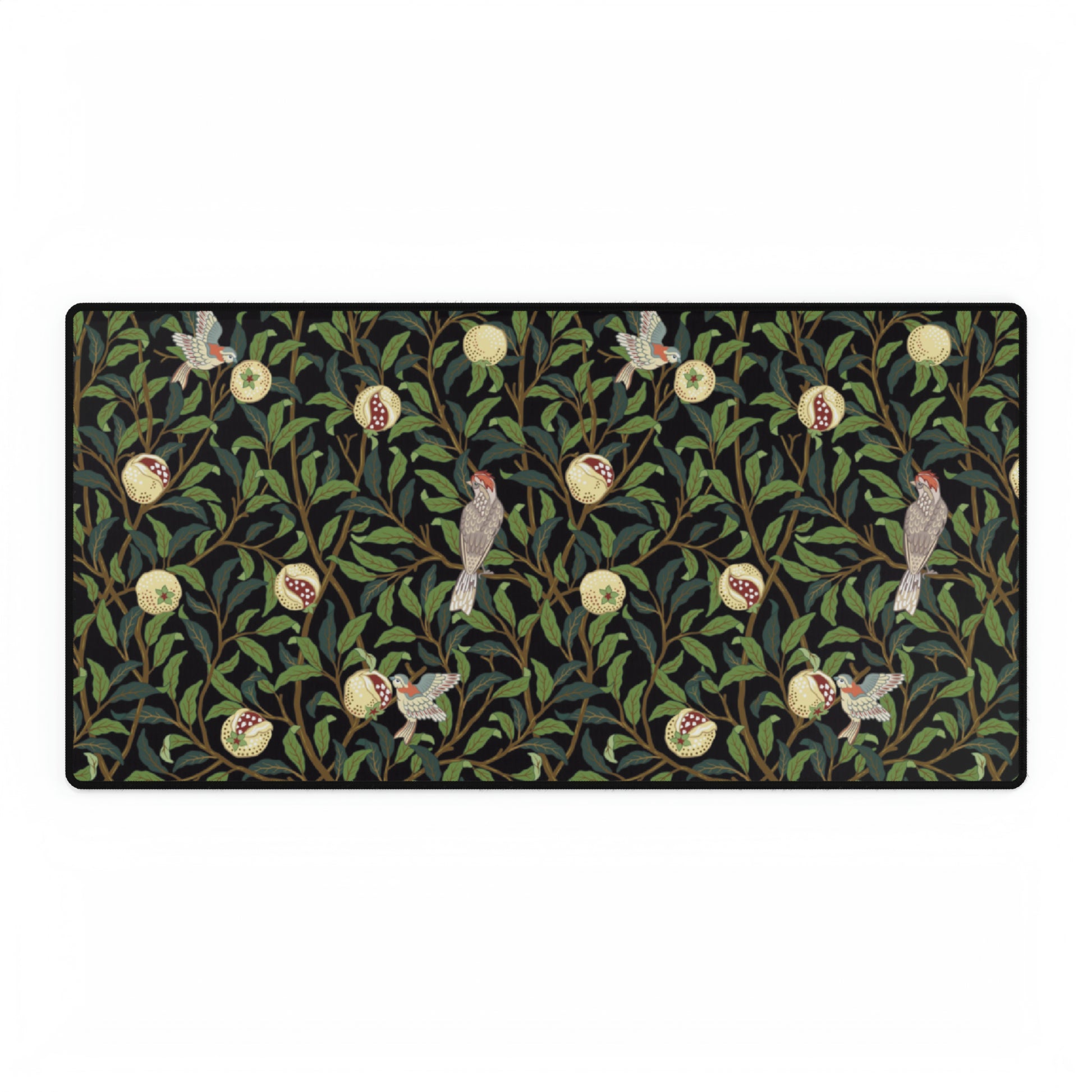 A rectangular desk mat with a floral William Morris & Co pattern featuring birds and pomegranates, placed under a desk with a keyboard and mouse on top.