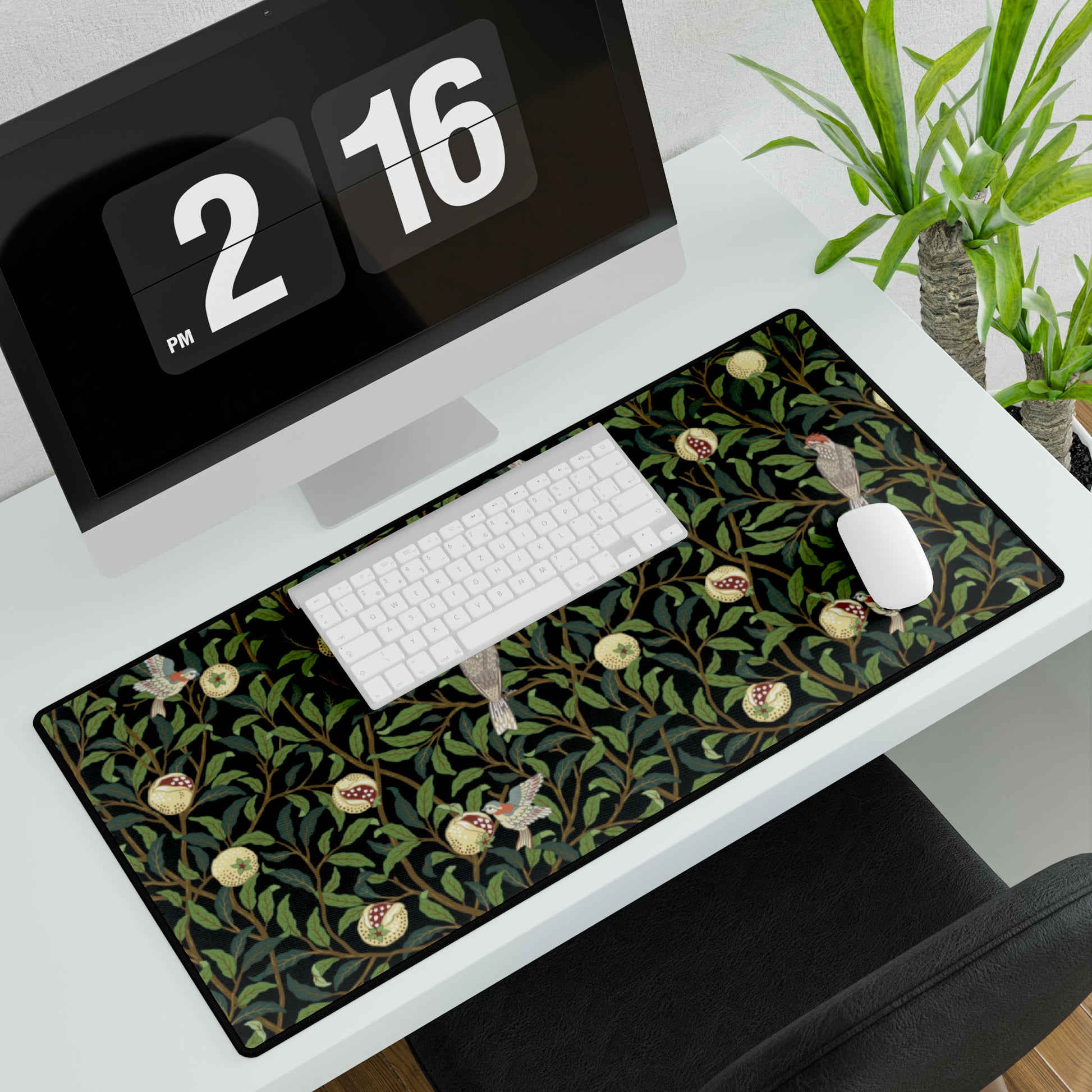A rectangular desk mat with a floral William Morris & Co pattern featuring birds and pomegranates, placed under a desk with a keyboard and mouse on top.