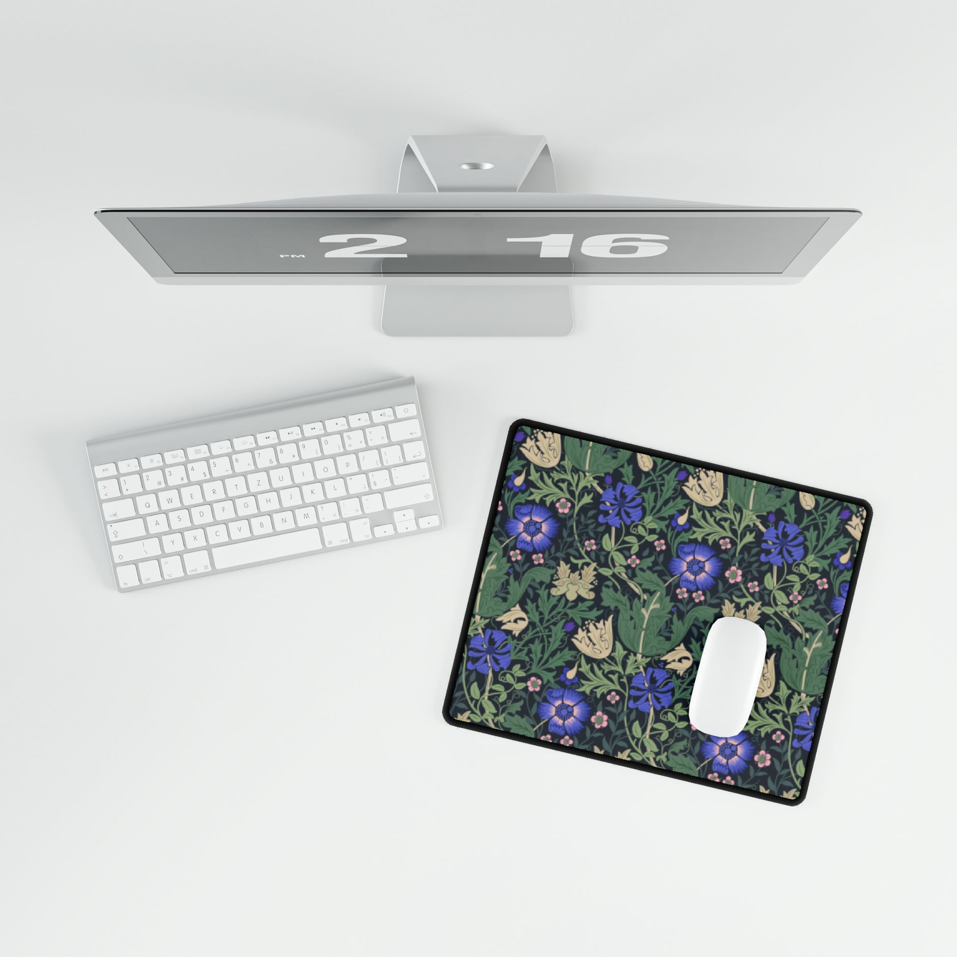 A desk mat with a William Morris & Co floral pattern, featuring a mouse pad on top. The desk mat has a non-slip base and is placed under a shelf with a computer monitor and a keyboard.