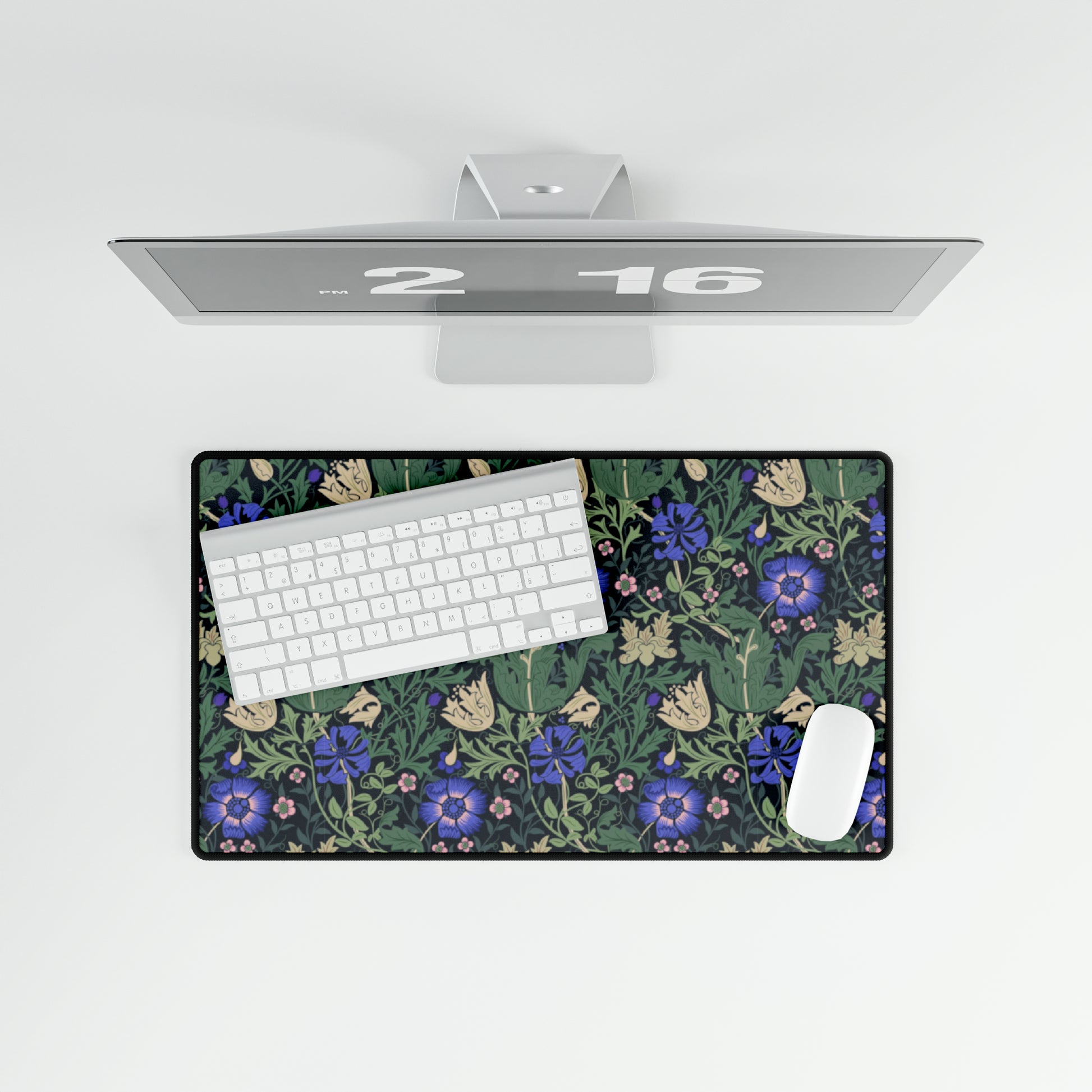A desk mat with a William Morris & Co floral pattern, featuring a mouse pad on top. The desk mat has a non-slip base and is placed under a shelf with a computer monitor and a keyboard.