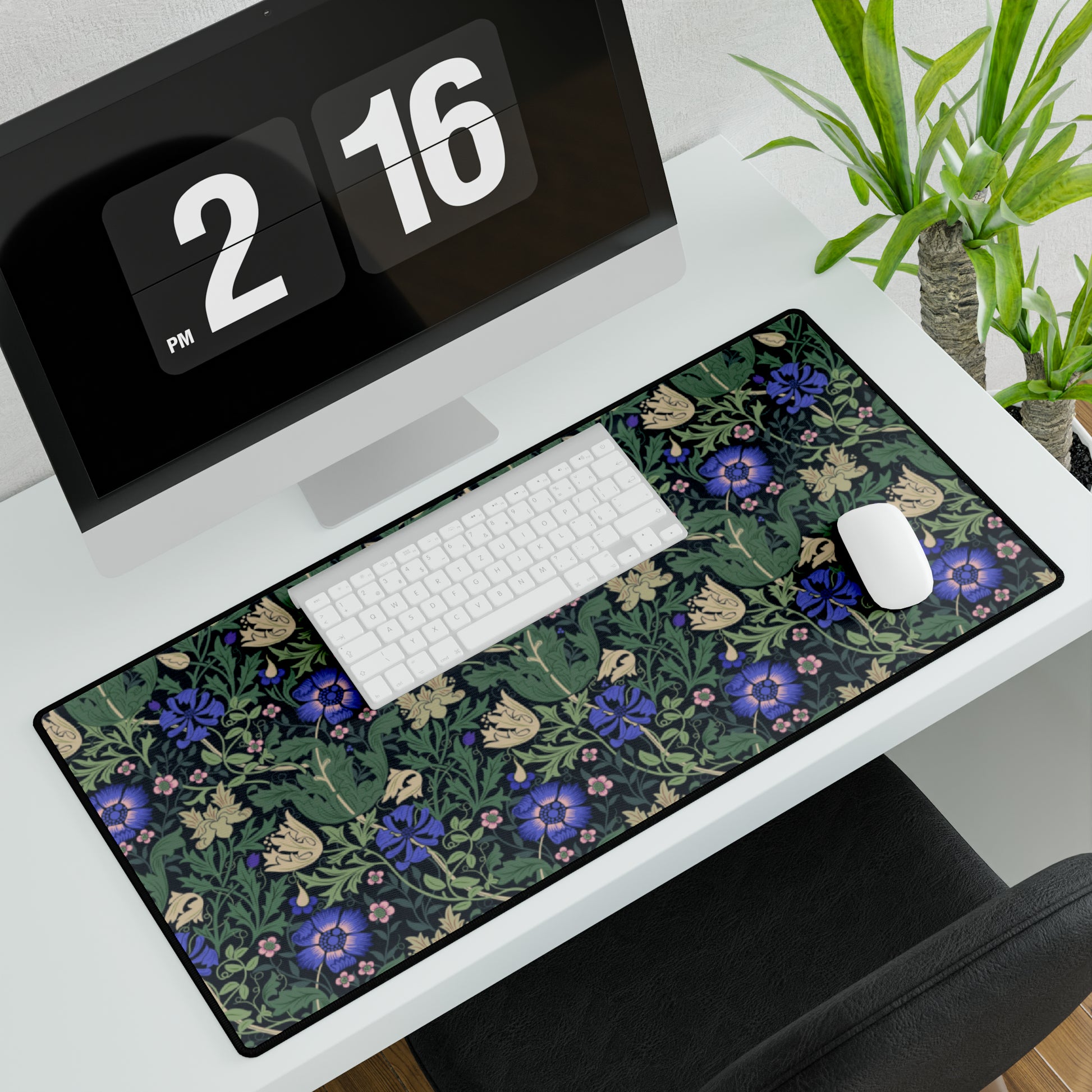 A desk mat with a William Morris & Co floral pattern, featuring a mouse pad on top. The desk mat has a non-slip base and is placed under a shelf with a computer monitor and a keyboard.