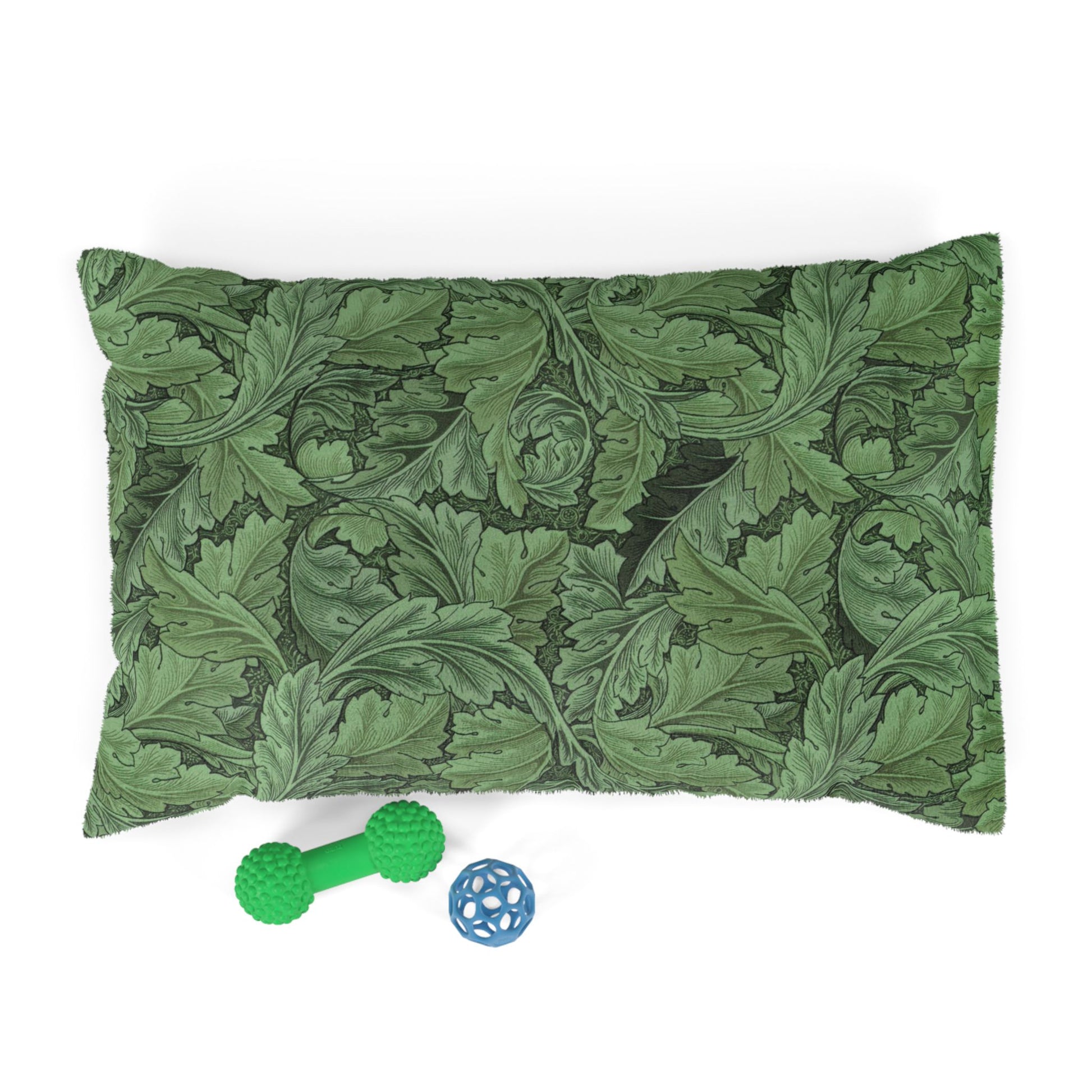 Green leaf-patterned pillow with a green rubber dog toy and blue ball on a white background