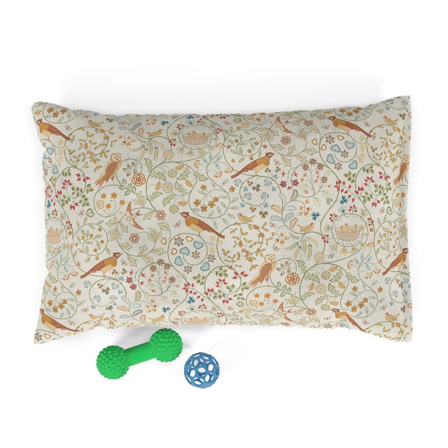 Decorative pillow with bird and floral pattern, accompanied by a green rubber dog toy and a blue ball on a white background.