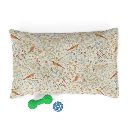 Decorative pillow with bird and floral pattern, accompanied by a green rubber dog toy and a blue ball on a white background.