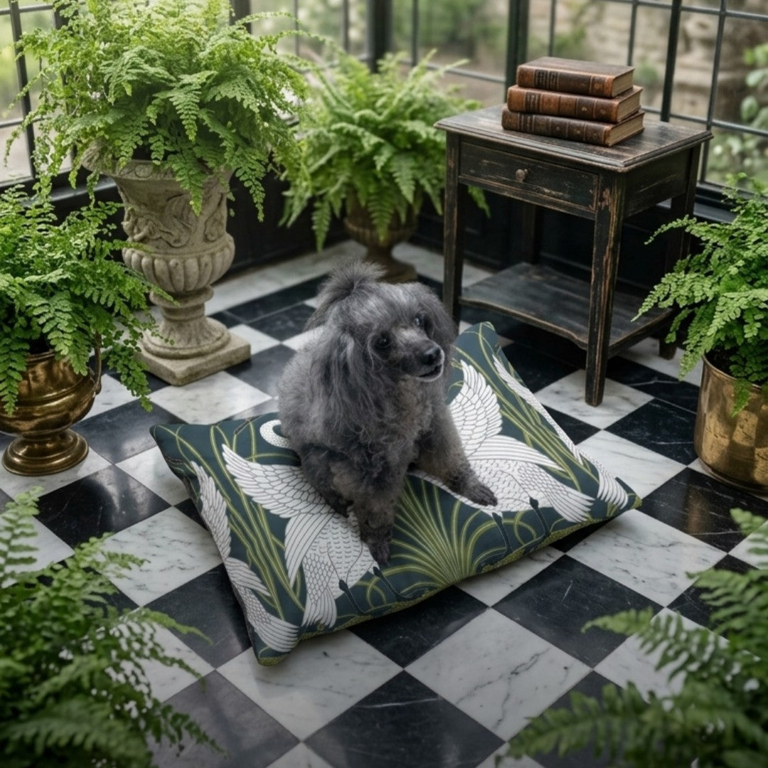 A small gray dog sits on a large decorative floor cushion with a green, white, and beige tropical leaf pattern, placed on a black-and-white checkered balcony floor surrounded by potted ferns.