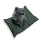 Dog sitting on a William Morris & Co patterned green cushion against a white background