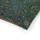 Dog sitting on a William Morris & Co patterned green cushion against a white background