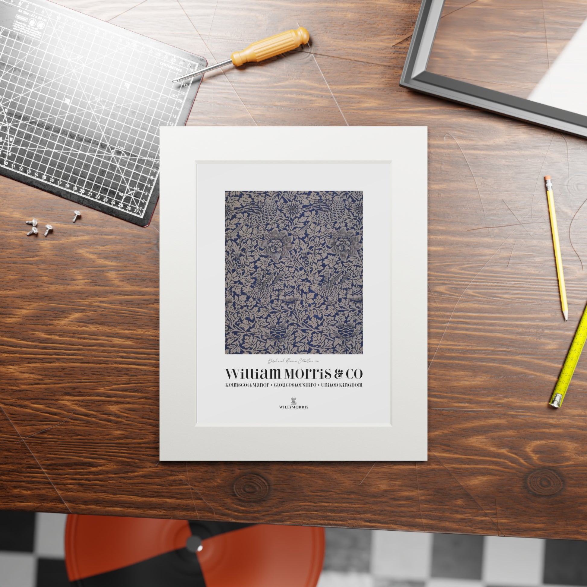 Framed artwork with 'William Morris & Co' on a wooden table with tools.