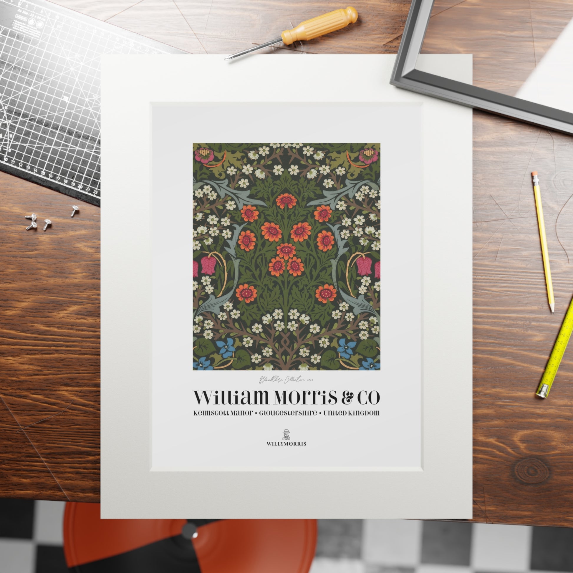 Framed floral pattern print by William Morris & Co on a wooden table with tools.