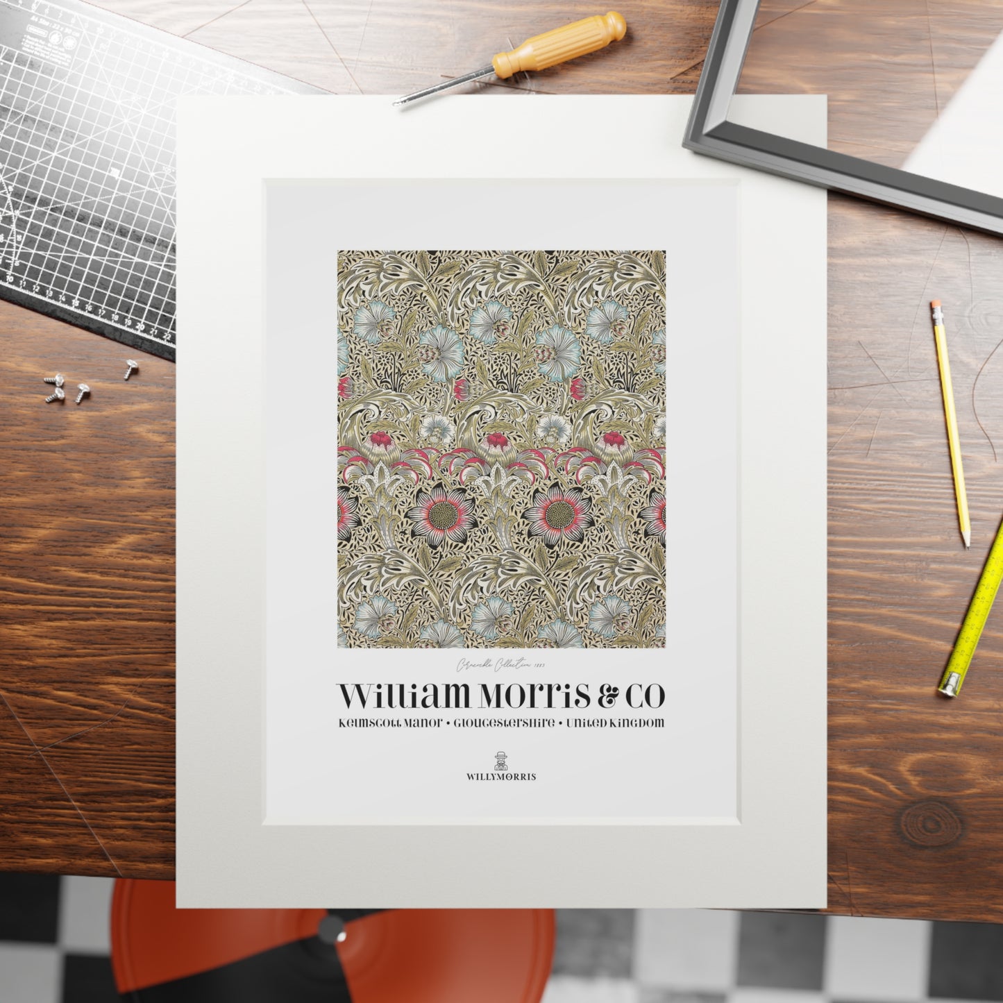 Framed pattern design with 'William Morris & Co' branding on a wooden table.
