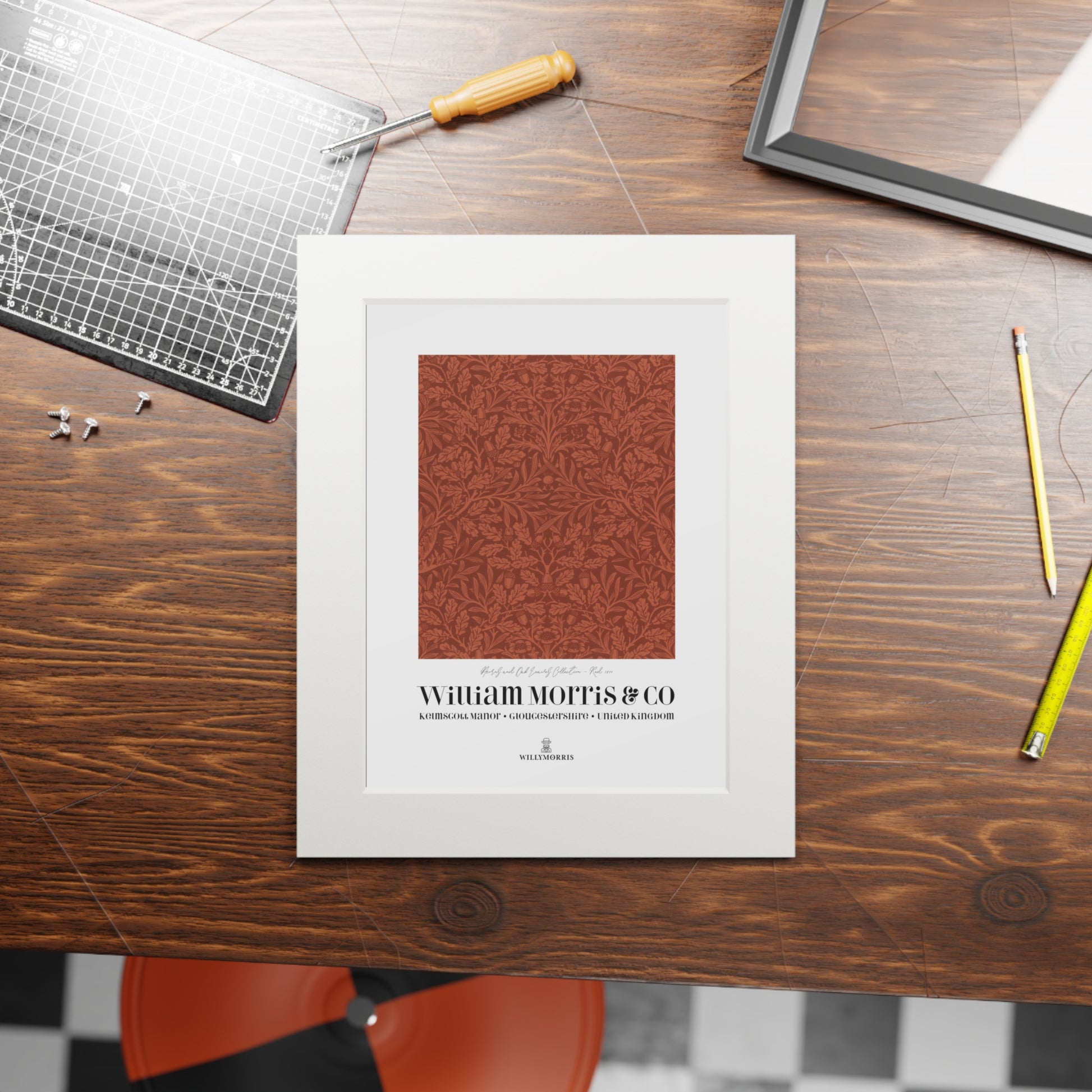 Framed artwork with a red pattern and 'William Morris & Co' text on a wooden table.