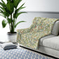 A plush fleece blanket with a floral William Morris & Co pattern featuring birds and pomegranates, predominantly in green tones.