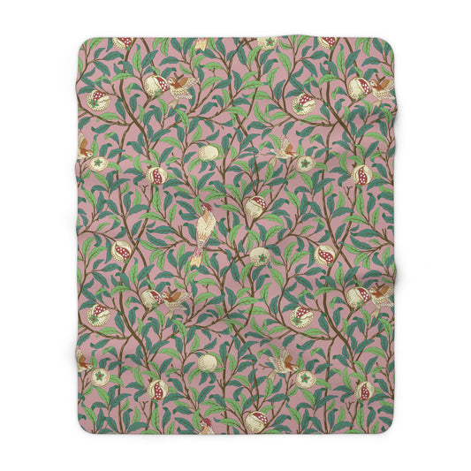 A plush fleece blanket with a floral William Morris & Co pattern featuring birds and pomegranate designs, predominantly in green and pink tones.