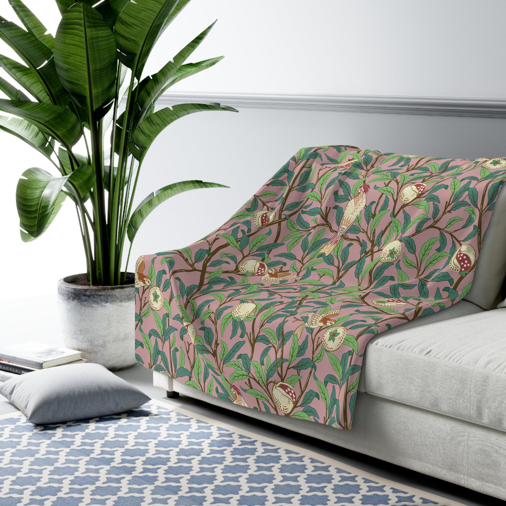 A plush fleece blanket with a floral William Morris & Co pattern featuring birds and pomegranate designs, predominantly in green and pink tones.