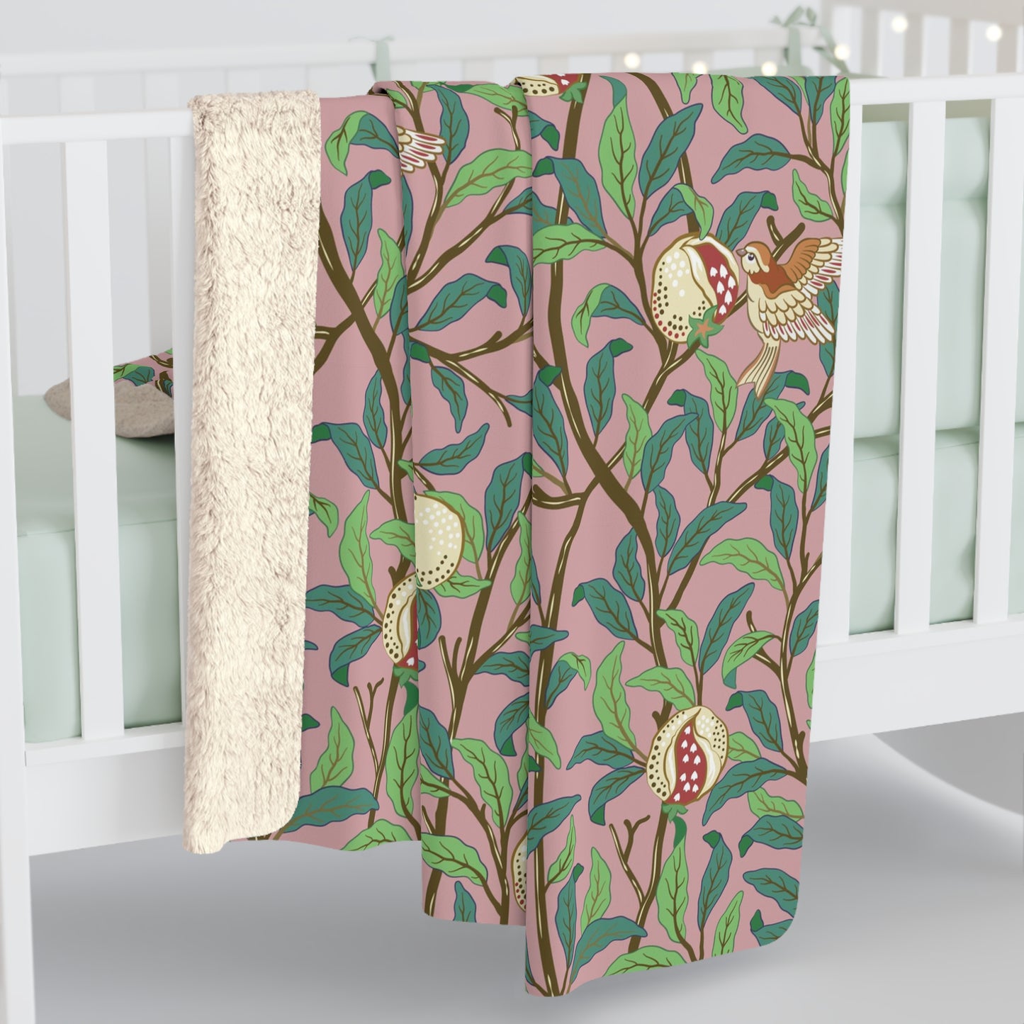A plush fleece blanket with a floral William Morris & Co pattern featuring birds and pomegranate designs, predominantly in green and pink tones.