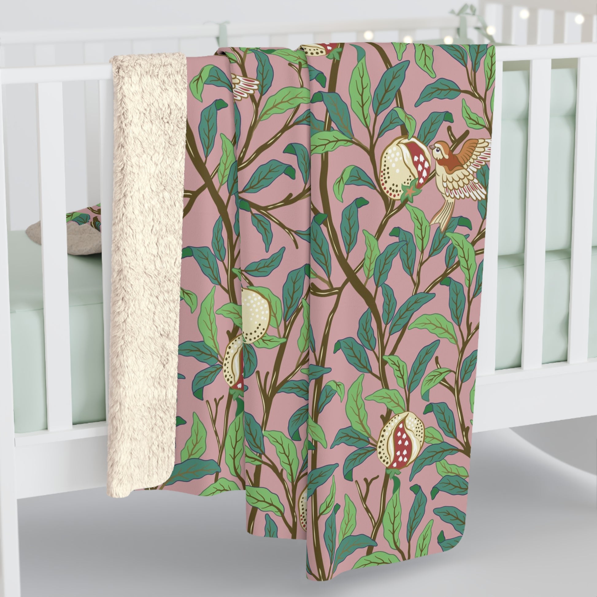 A plush fleece blanket with a floral William Morris & Co pattern featuring birds and pomegranate designs, predominantly in green and pink tones.