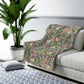 A plush fleece blanket with a floral William Morris & Co pattern featuring birds and pomegranate designs, predominantly in green and pink tones.