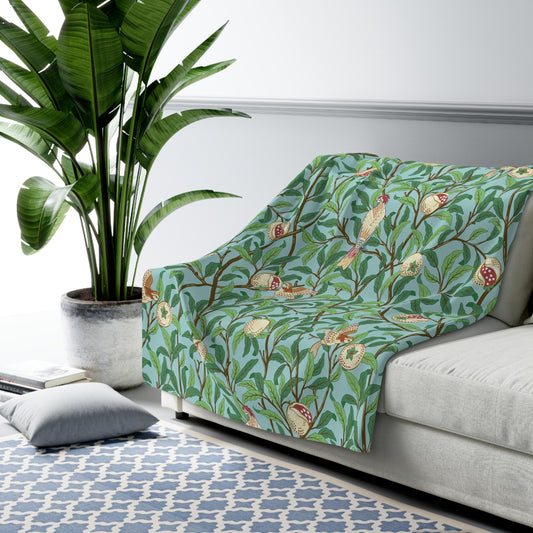 A Sherpa fleece blanket with an all-over print of birds and pomegranate fruits inspired by William Morris & Co on a blue background.