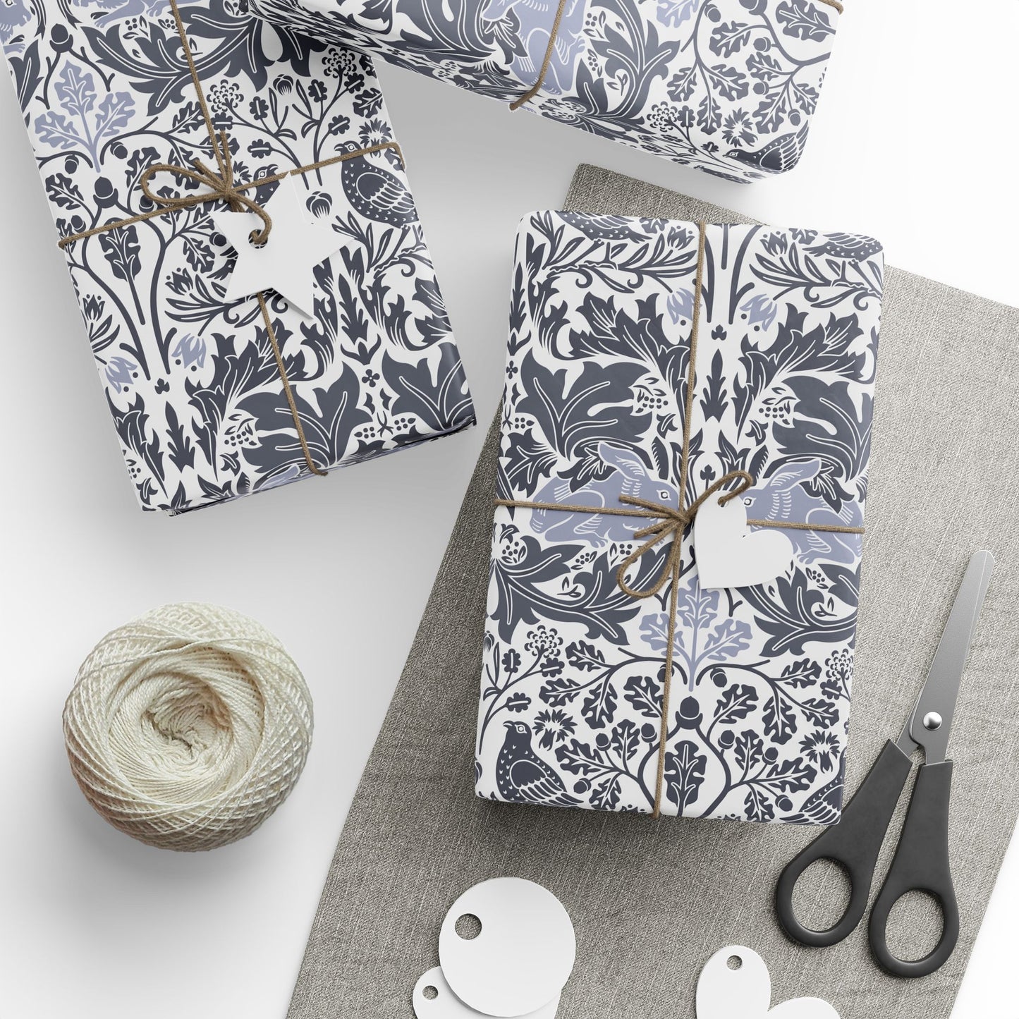Gifts wrapped in blue and white floral patterned paper with scissors and twine on a white surface.