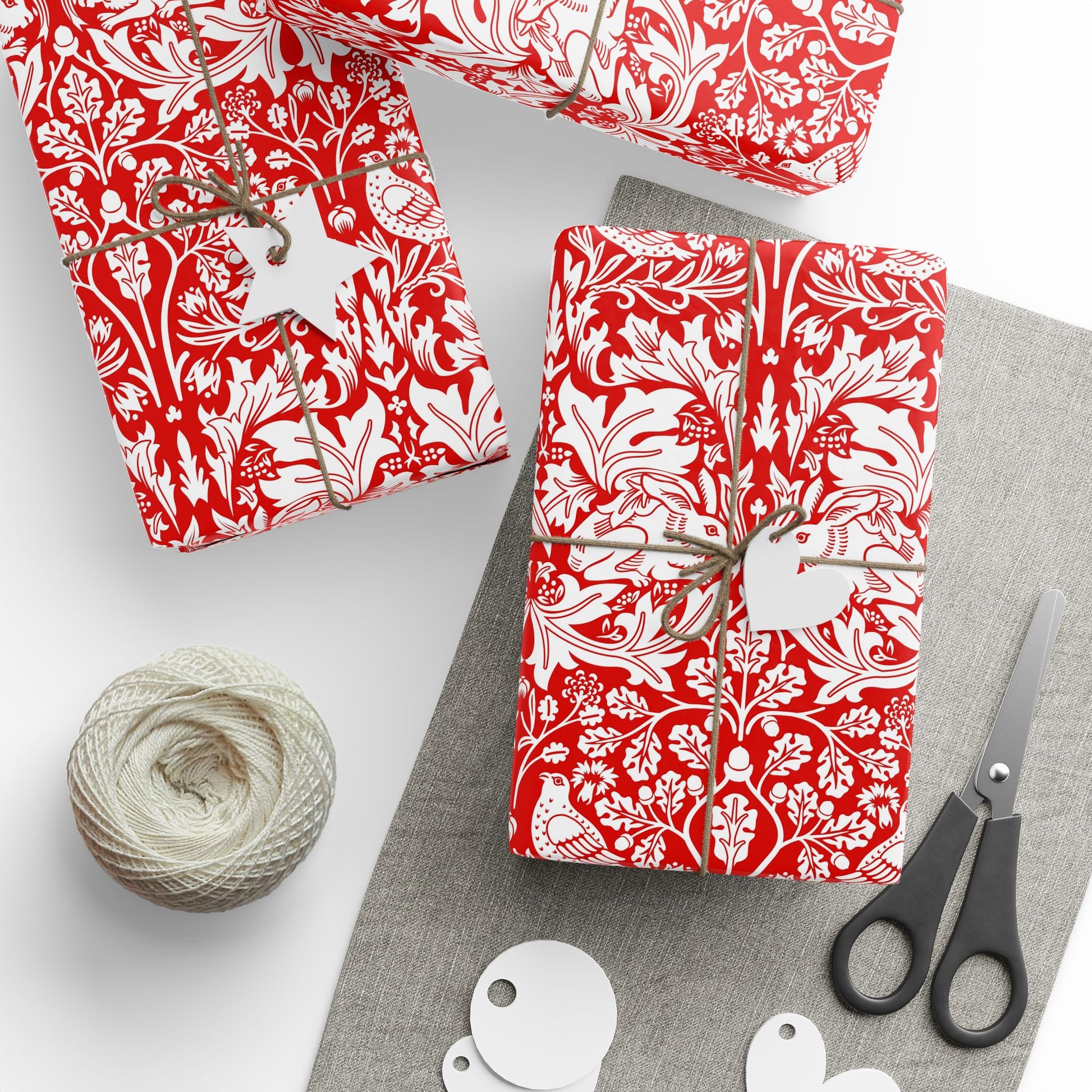 Gifts wrapped in red and white patterned paper with scissors and yarn on a gray surface.