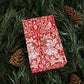 Red and white patterned gift box on green foliage with pine cones