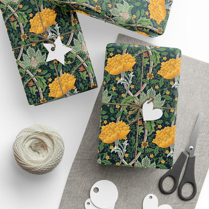 Floral-patterned gift wrap with yellow flowers and green leaves, tied with twine and a tag, on a white surface with scissors and yarn.