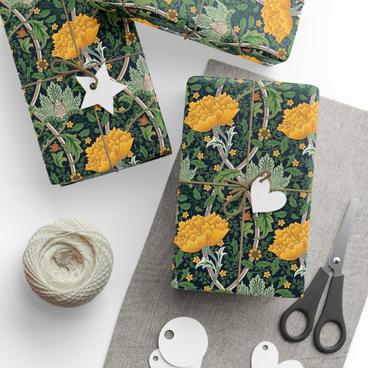 Floral-patterned gift wrap with yellow flowers and green leaves, tied with twine and a tag, on a white surface with scissors and yarn.