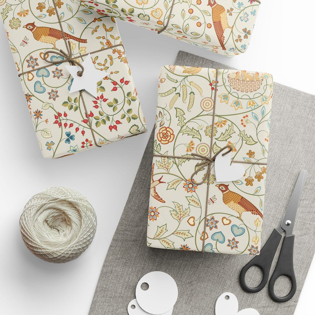 Gifts wrapped in decorative paper with a bird and floral pattern, accompanied by scissors and twine on a white surface.
