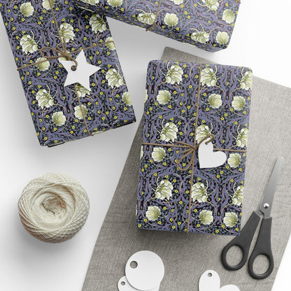 Gift wrap with floral pattern, scissors, yarn, and tags on a white surface