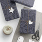 Gift boxes wrapped in dark blue patterned paper with decorative tags and scissors on a light surface.
