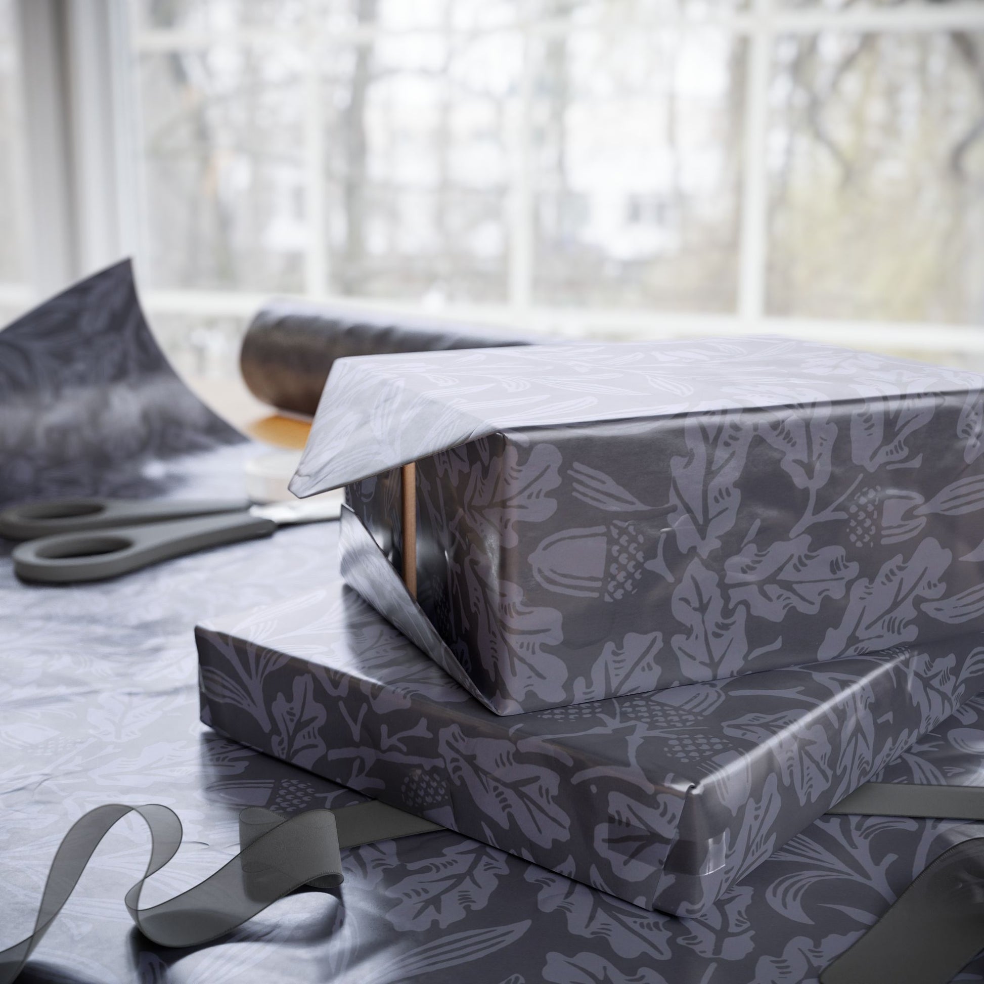 Two wrapped presents with floral pattern on a table with scissors in the background.