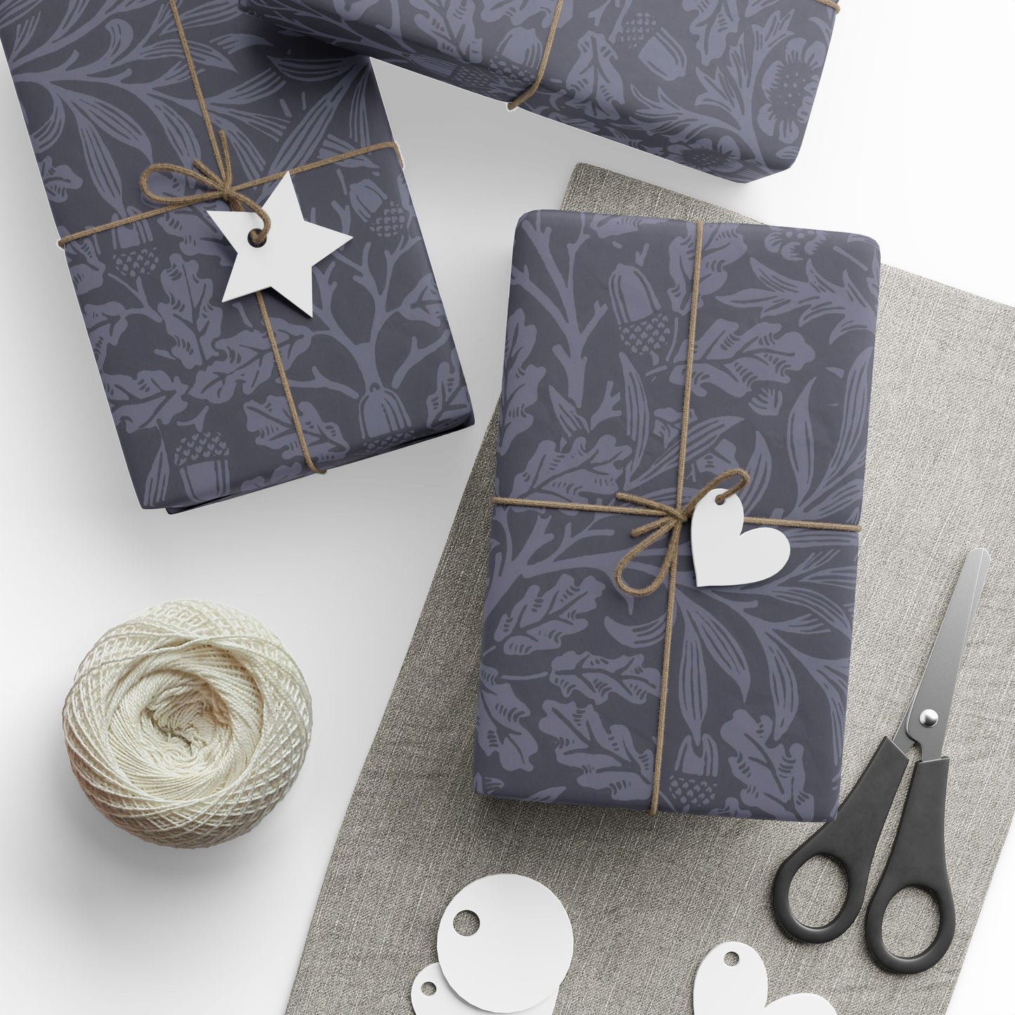 Gift boxes wrapped in dark blue patterned paper with decorative tags and scissors on a light surface.