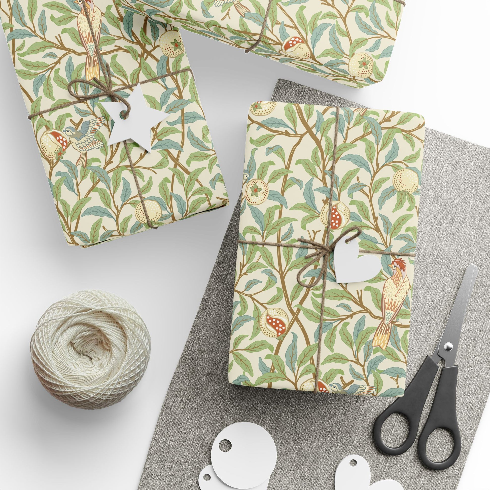 Gift boxes wrapped in decorative paper with birds and branches, scissors, and yarn on a white surface.