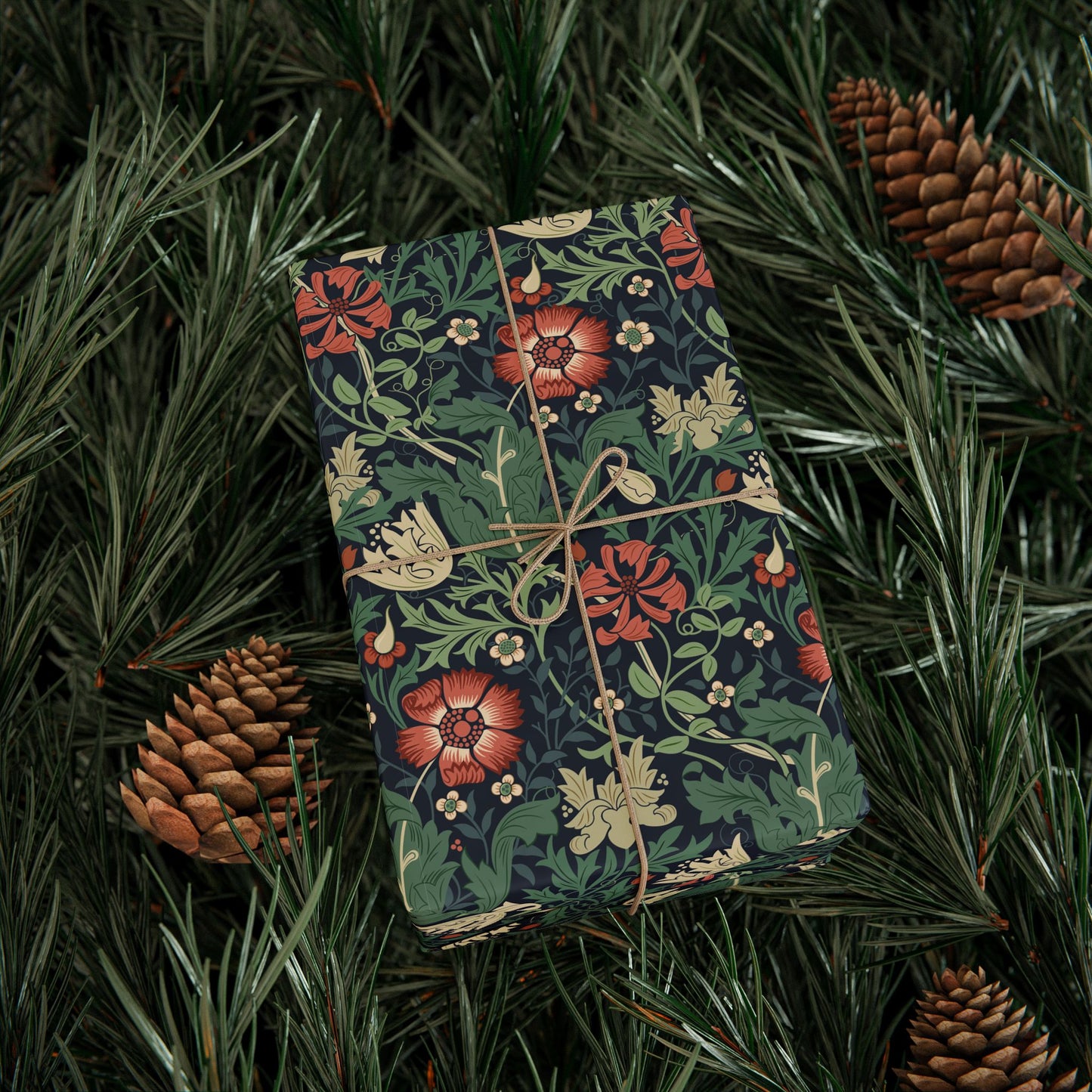 Floral-patterned gift box tied with string on a bed of pine needles and pine cones.