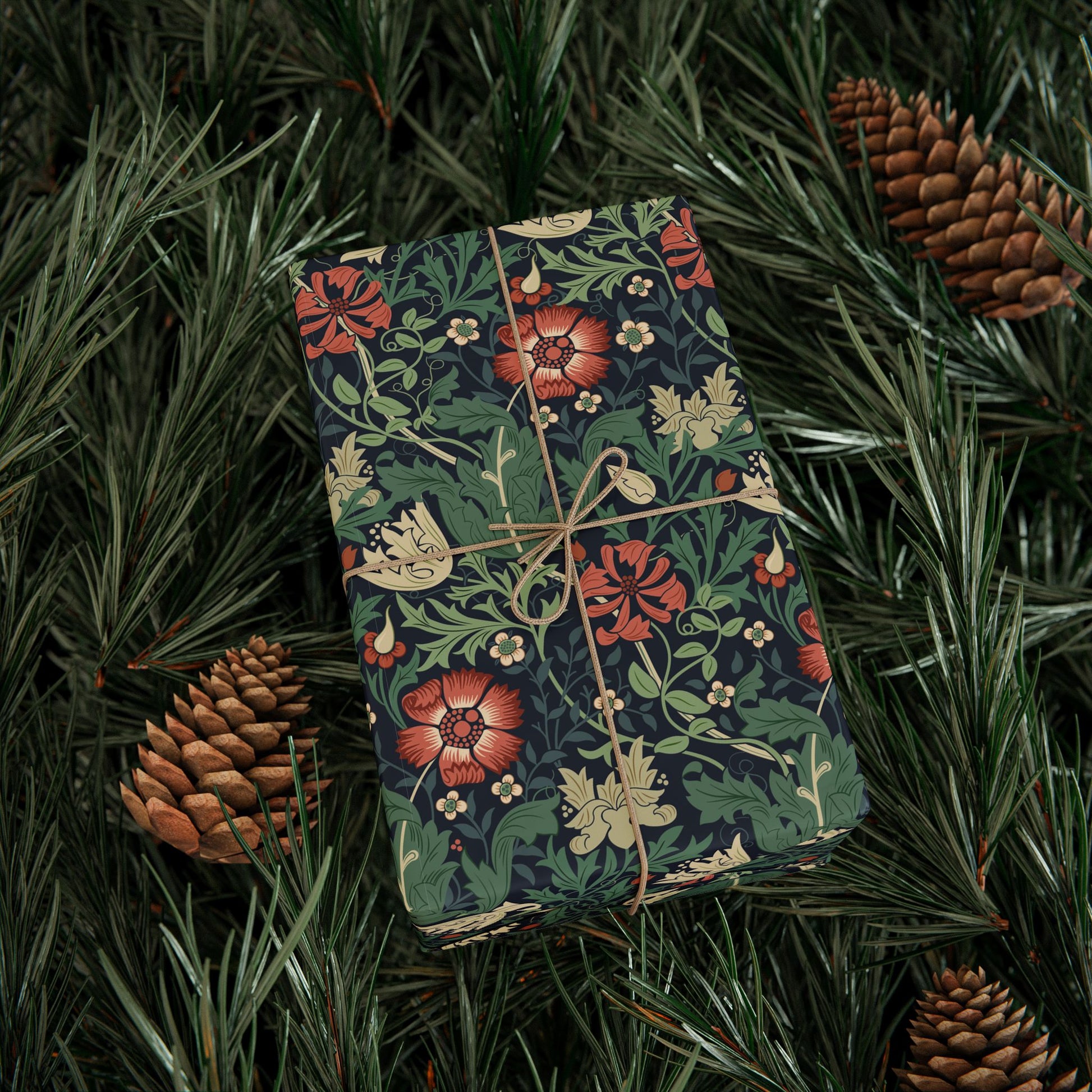 Floral-patterned gift box tied with string on a bed of pine needles and pine cones.