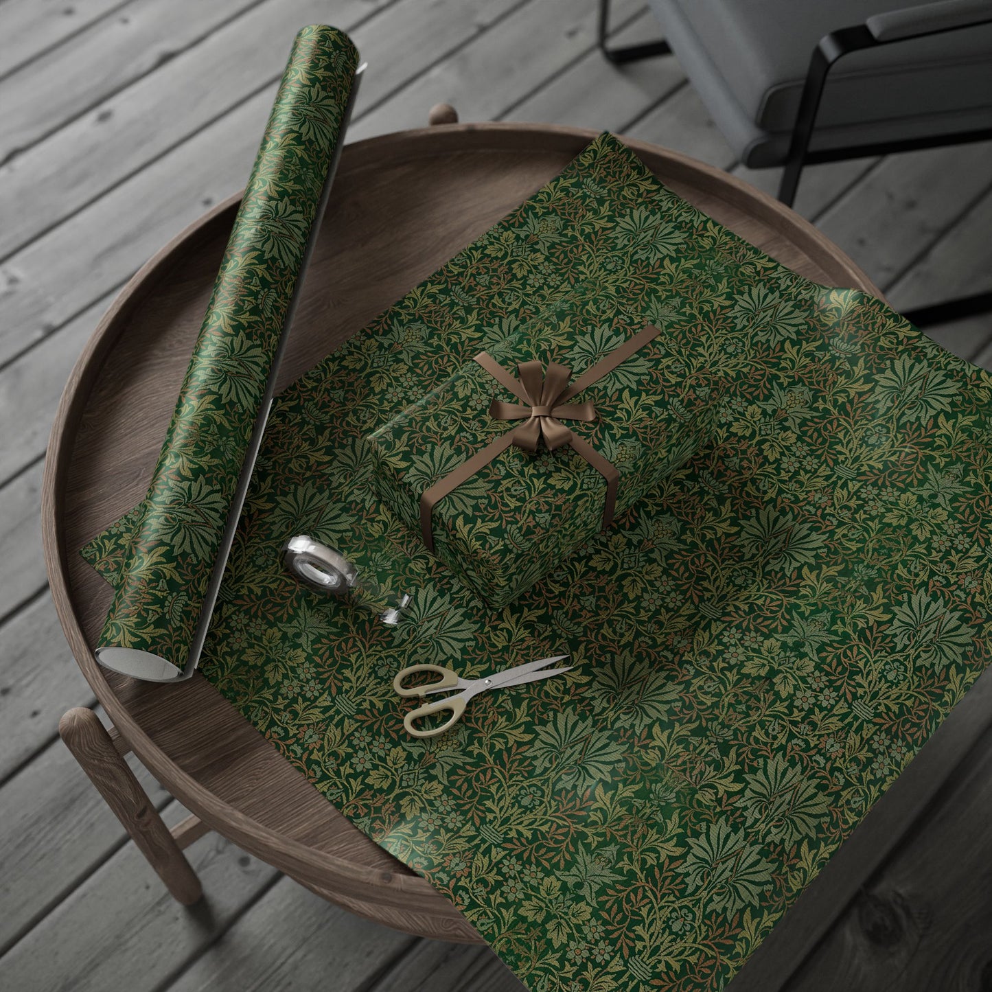 Green floral-patterned gift wrap with scissors and a roll on a wooden surface