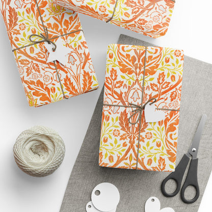 Gift boxes wrapped in orange and yellow floral paper with scissors and yarn on a white surface