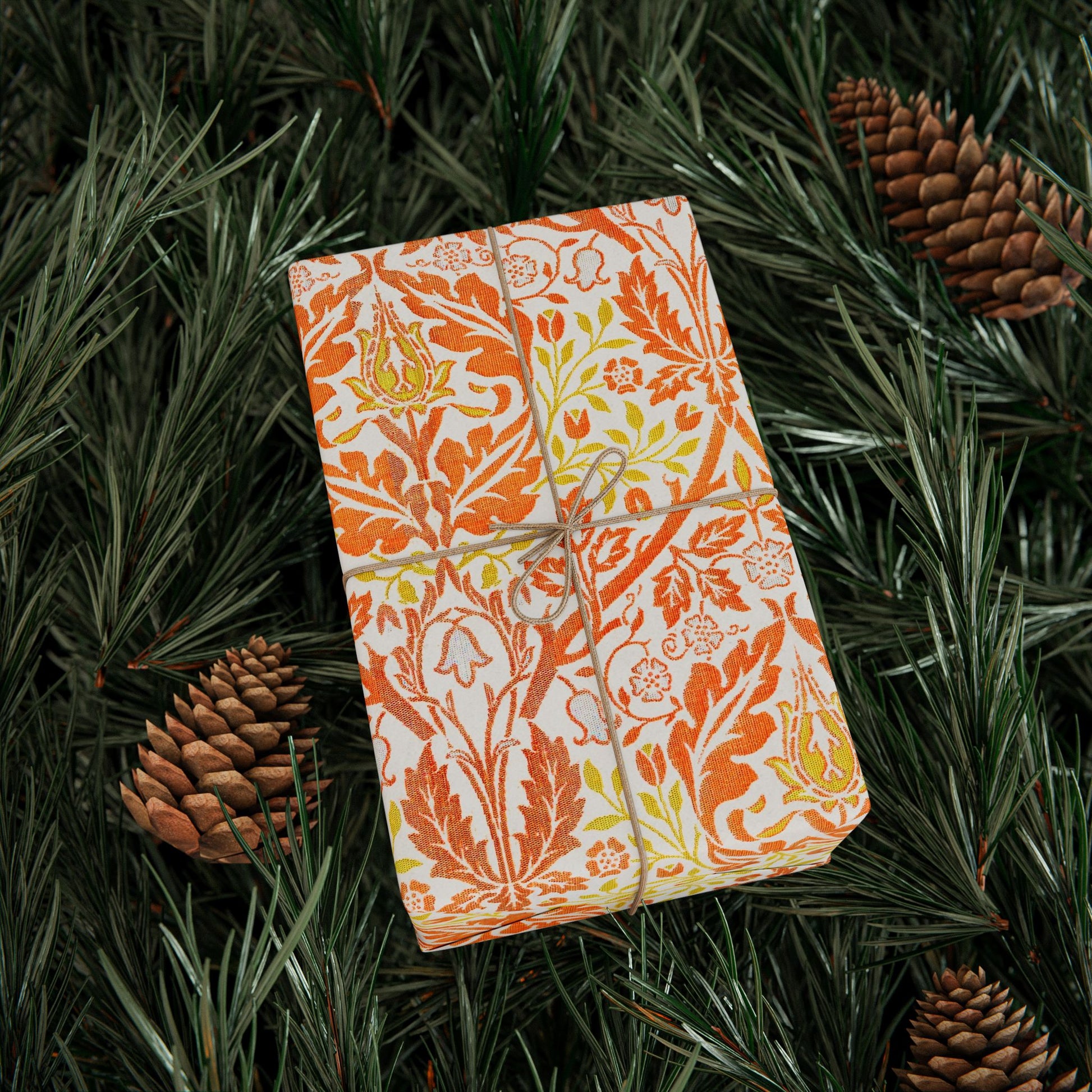Gift wrapped in orange floral paper with twine on green foliage
