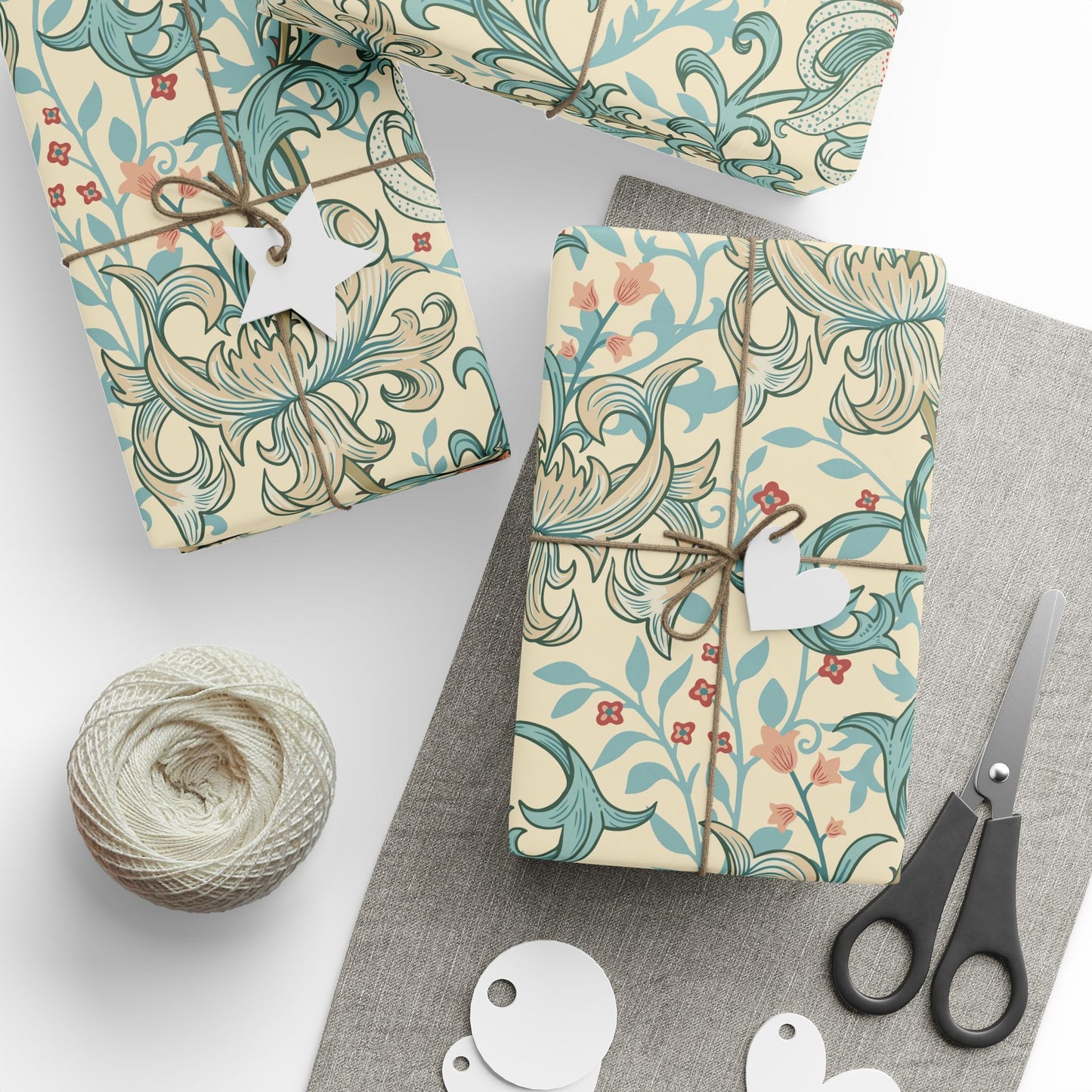 Gift boxes wrapped in decorative paper with a floral pattern, scissors, and twine on a gray surface.