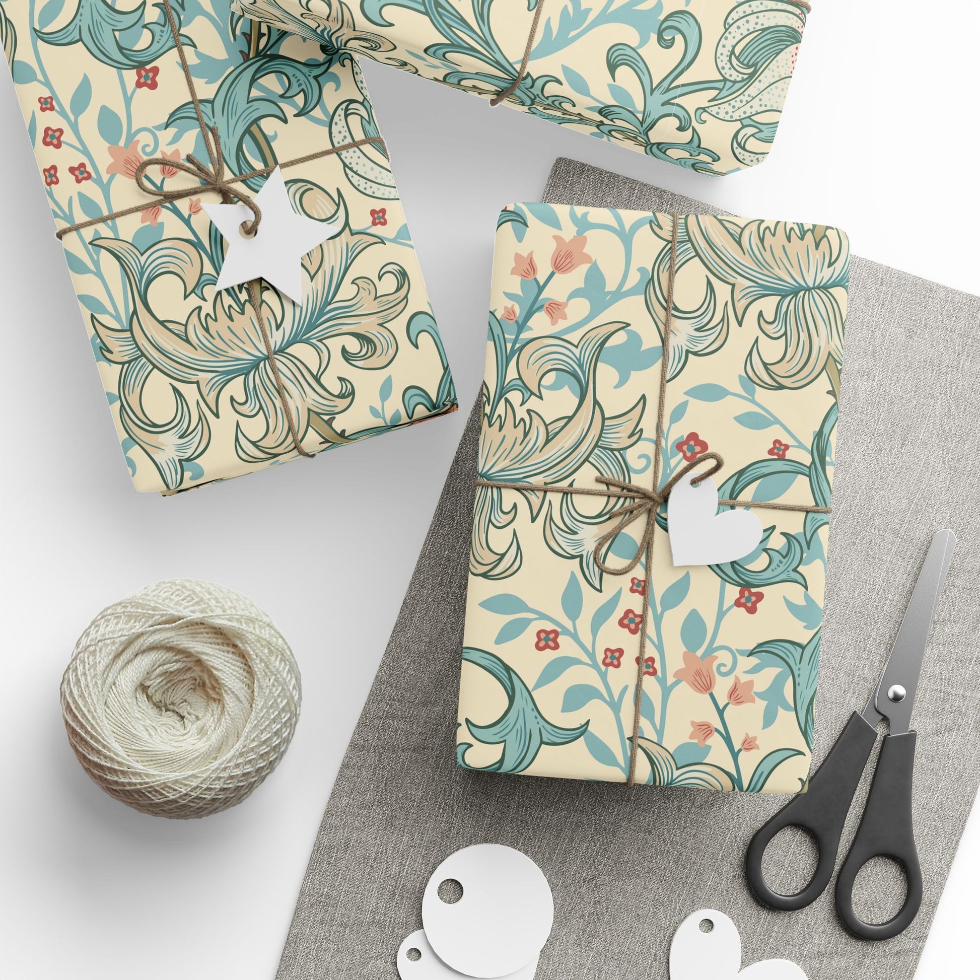 Gift boxes wrapped in decorative paper with a floral pattern, scissors, and twine on a gray surface.