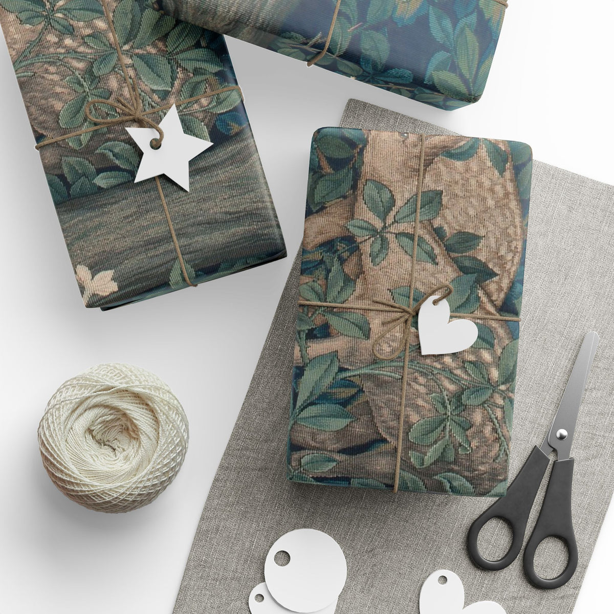 Gift boxes wrapped in nature-themed paper with decorative tags and scissors on a white surface.