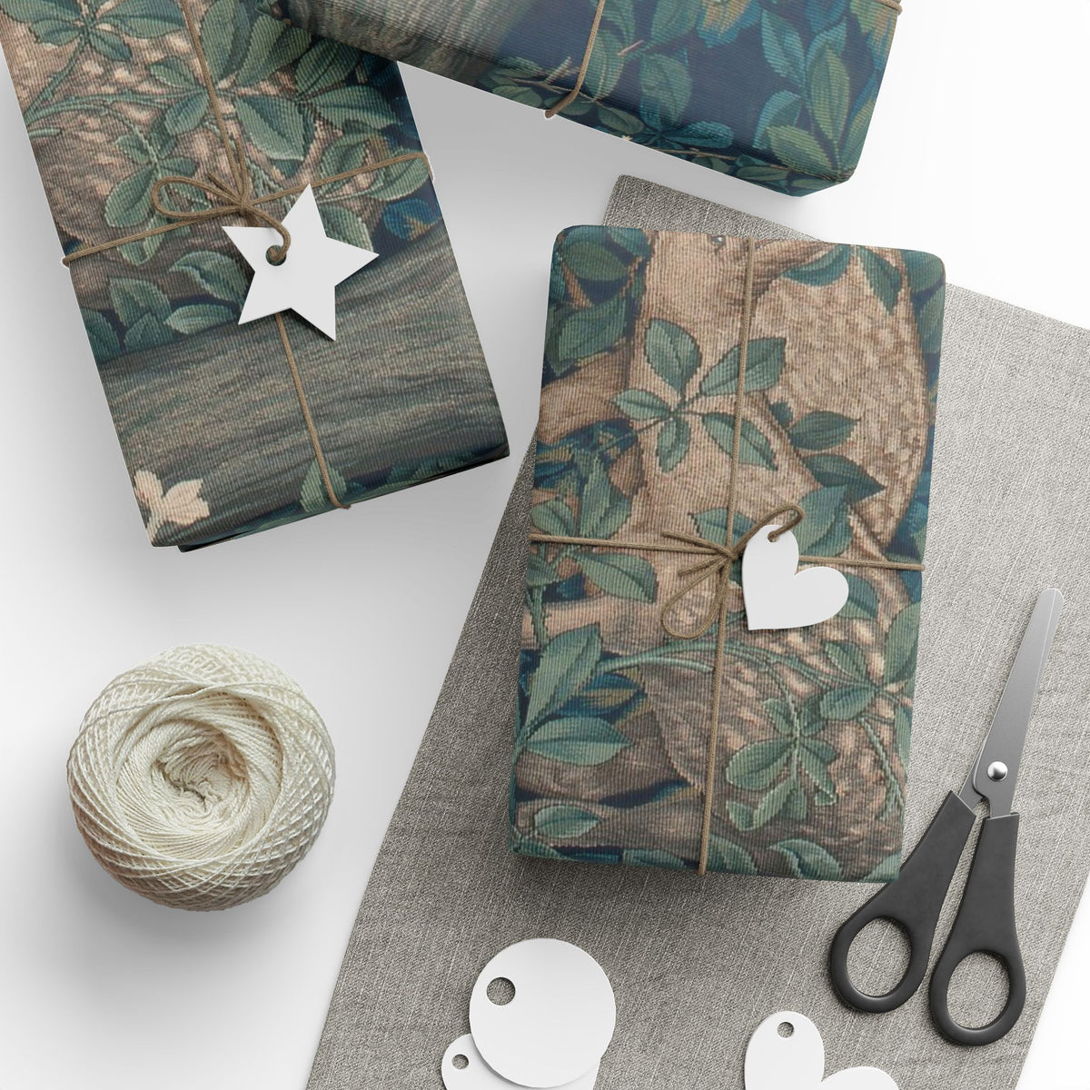 Gift boxes wrapped in nature-themed paper with decorative tags and scissors on a white surface.