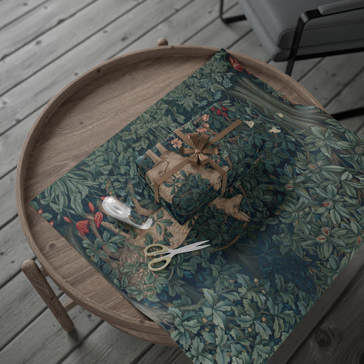 Wooden tray with a green floral-patterned wrapping paper, fabric, scissors, and a spool of thread on a wooden surface.