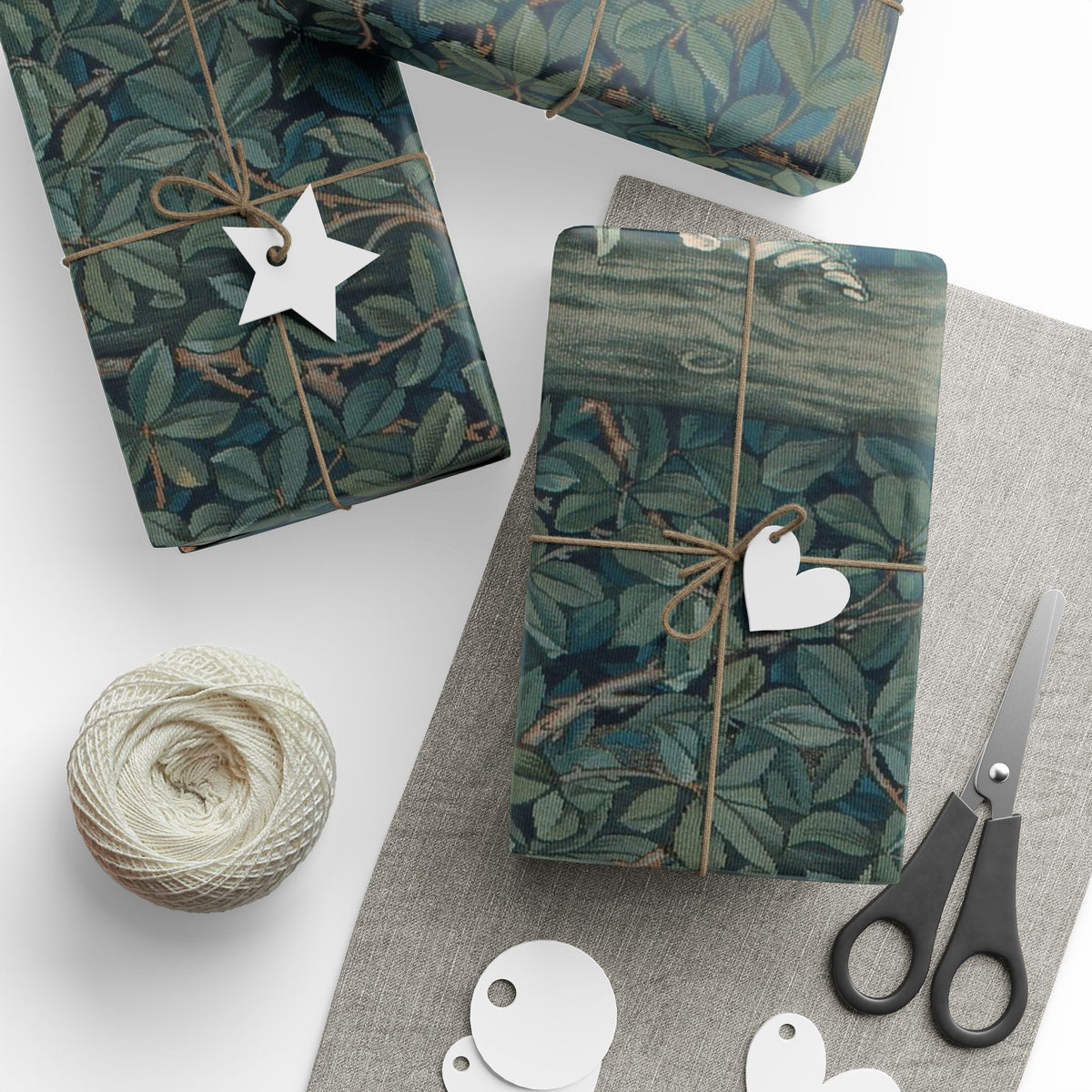 Gift boxes wrapped in green leaf-patterned paper with decorative tags and scissors on a white surface.