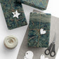 Gift boxes wrapped in green leaf-patterned paper with decorative tags and scissors on a white surface.