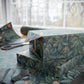 Stack of wrapped presents with green leaf pattern on a table with scissors and additional wrapping paper.