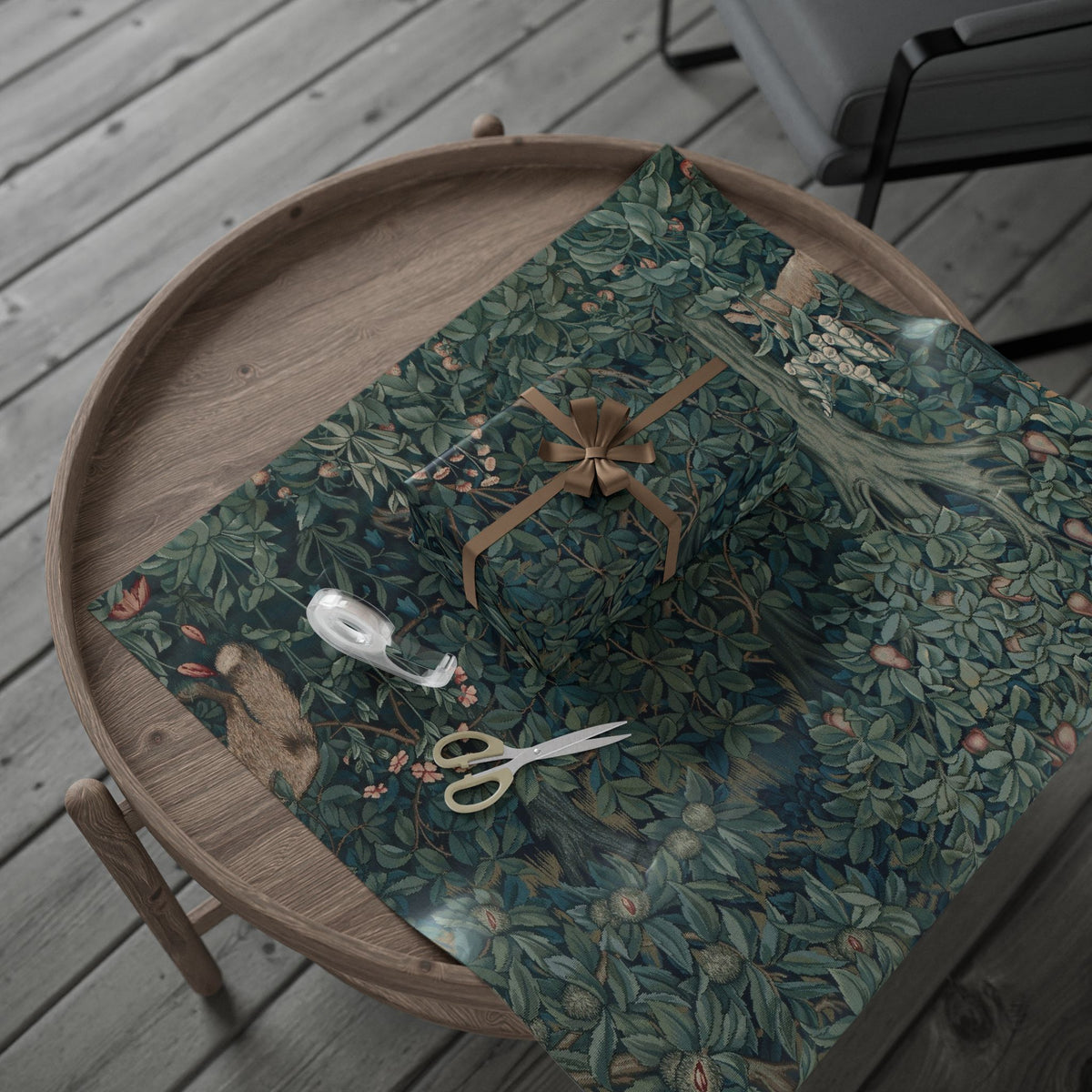 Wooden tray with a green floral patterned cloth, scissors, and a spool of thread on a wooden surface.