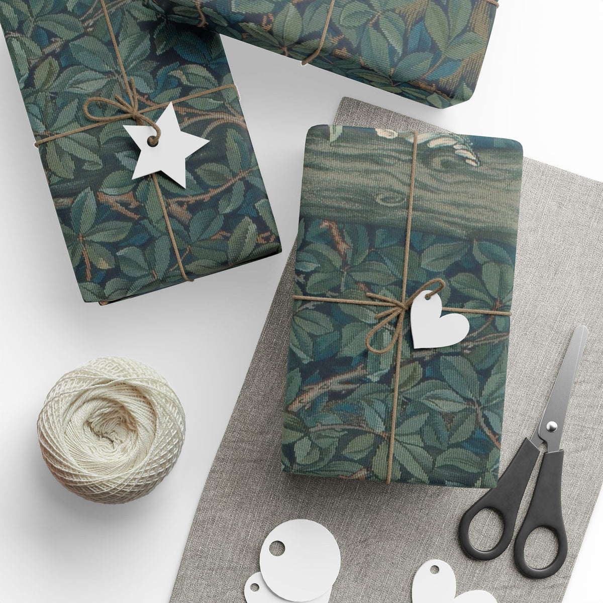 Gift boxes wrapped in green leaf-patterned paper with decorative tags and scissors on a white surface.
