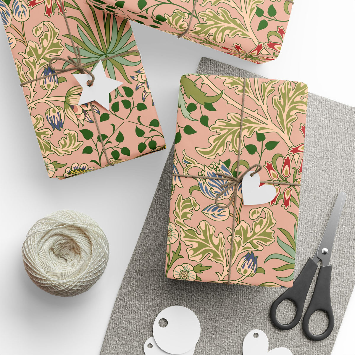 Gift wrap with floral pattern, scissors, yarn, and tags on a gray surface.